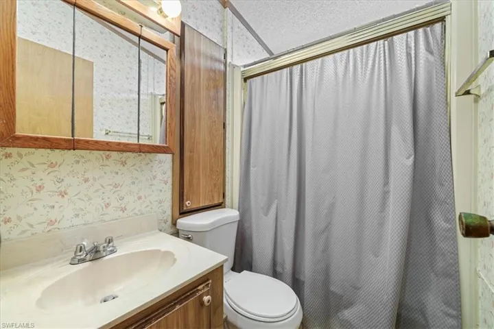 Full bath with wallpapered walls, a shower with shower curtain, vanity, and a textured ceiling