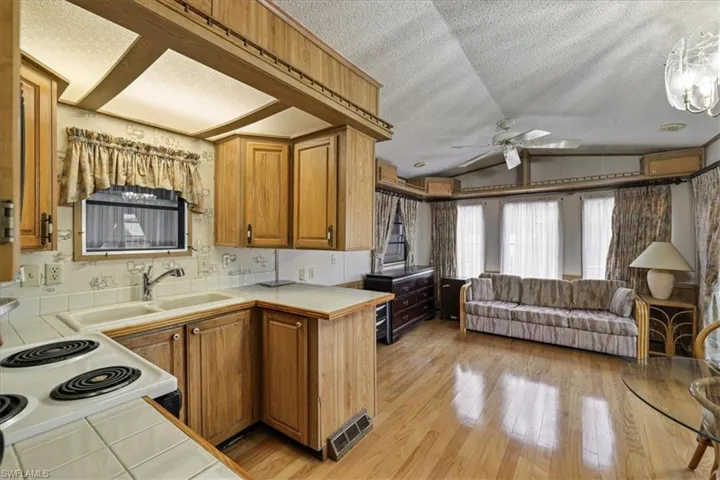 Kitchen featuring vaulted ceiling, brown cabinets, a textured ceiling, open floor plan, and tile countertops