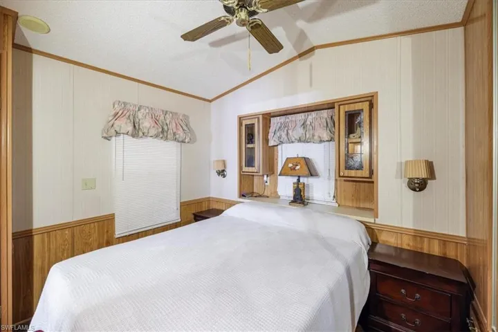 Bedroom with wood walls, wainscoting, vaulted ceiling, a textured ceiling, and a ceiling fan