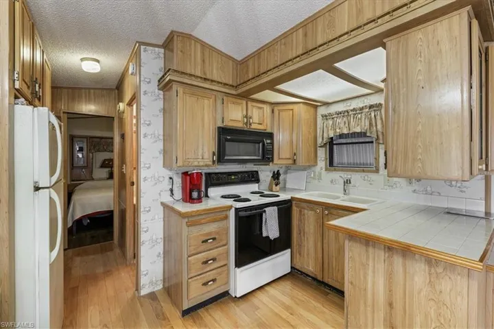 Kitchen featuring tile countertops, range with electric cooktop, wallpapered walls, a textured ceiling, and freestanding refrigerator