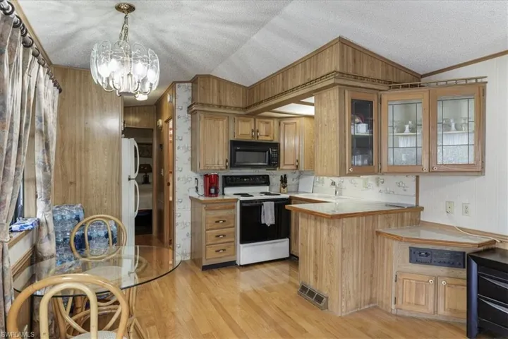 Kitchen featuring electric range oven, light wood-style flooring, glass insert cabinets, vaulted ceiling, and hanging light fixtures