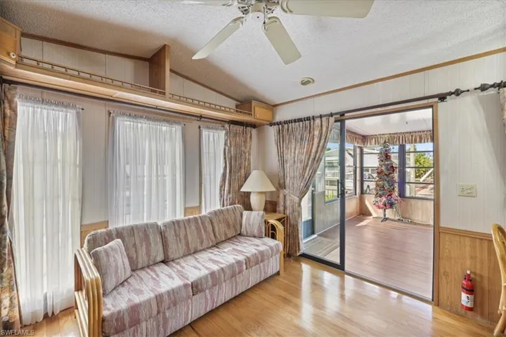 Living room with a textured ceiling, lofted ceiling, wooden walls, wood finished floors, and crown molding