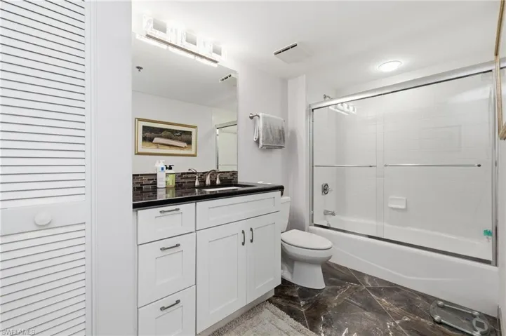 Bathroom featuring a closet, vanity, shower / bath combination with glass door, and dark marble finish flooring