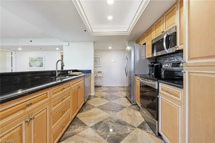 Kitchen with appliances with stainless steel finishes, dark stone countertops, recessed lighting, decorative backsplash, and a tray ceiling