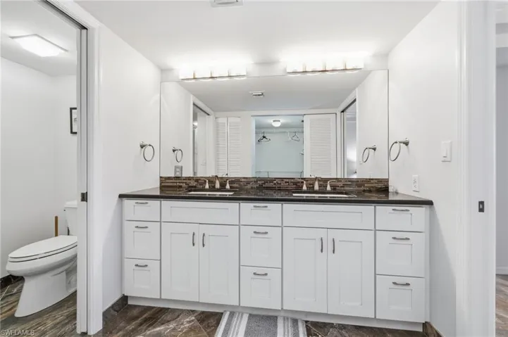 Bathroom with double vanity, a closet, backsplash, and dark marble finish floors