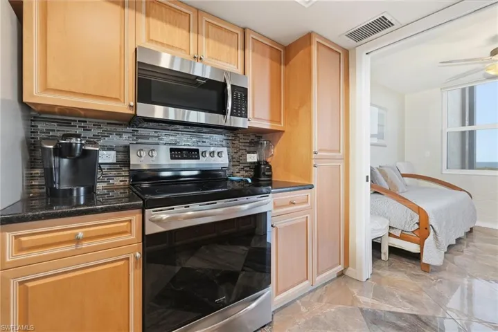 Kitchen featuring stainless steel appliances, decorative backsplash, dark stone counters, and light brown cabinetry