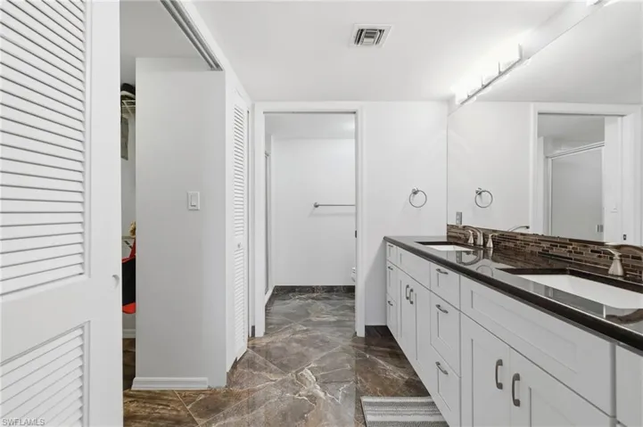 Full bathroom featuring double vanity, dark marble finish floors, a shower with shower door, and a walk in closet
