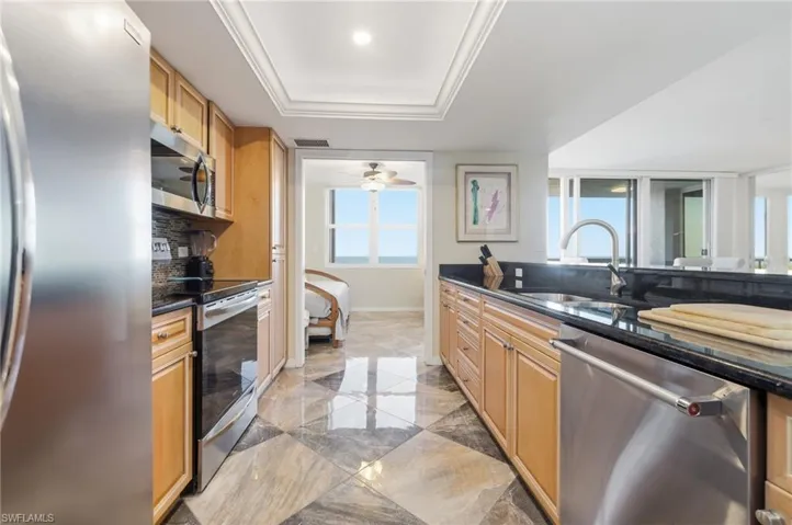 Kitchen with appliances with stainless steel finishes, dark stone counters, light marble finish floors, a raised ceiling, and ceiling fan