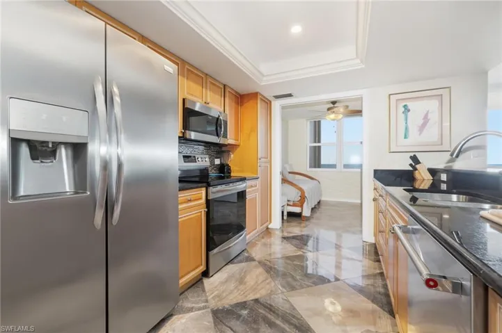 Kitchen featuring appliances with stainless steel finishes, dark stone counters, a tray ceiling, ceiling fan, and dark marble finish floors