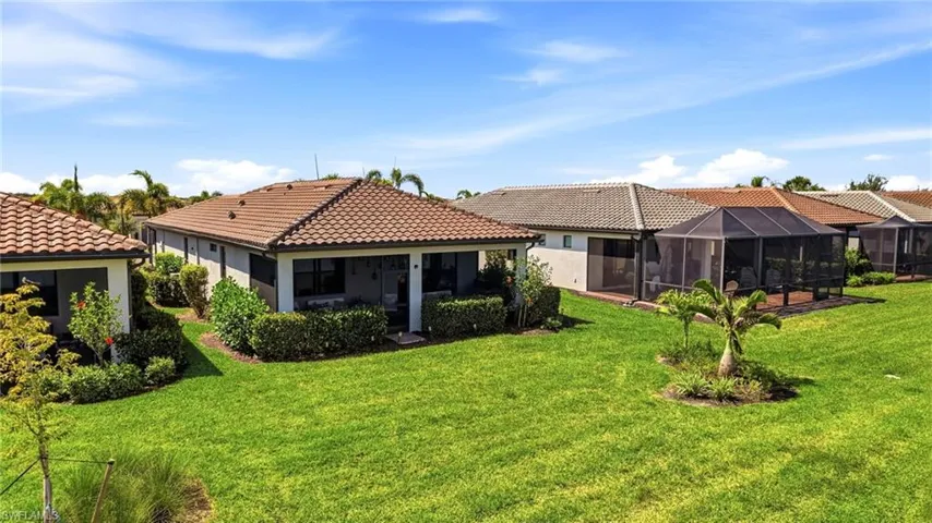 Expansive backyard featuring a manicured lawn, mature landscaping, and an enclosed screened lanai