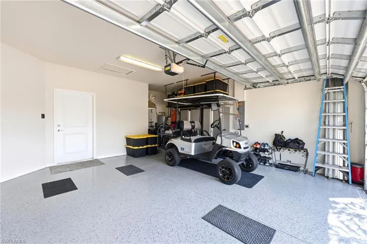 Spacious garage featuring a light gray speckled epoxy floor, white interior access door, bright overhead lighting, and an automatic garage door opener