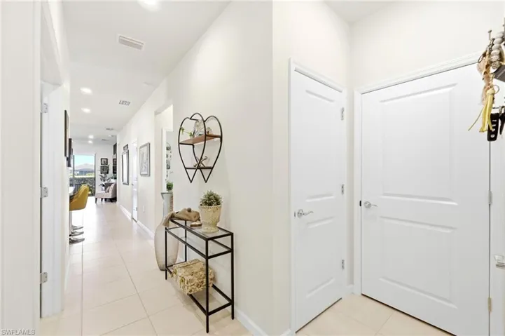 Bright, neutral-toned hallway featuring recessed lighting, light tile flooring, and multiple white panel doors