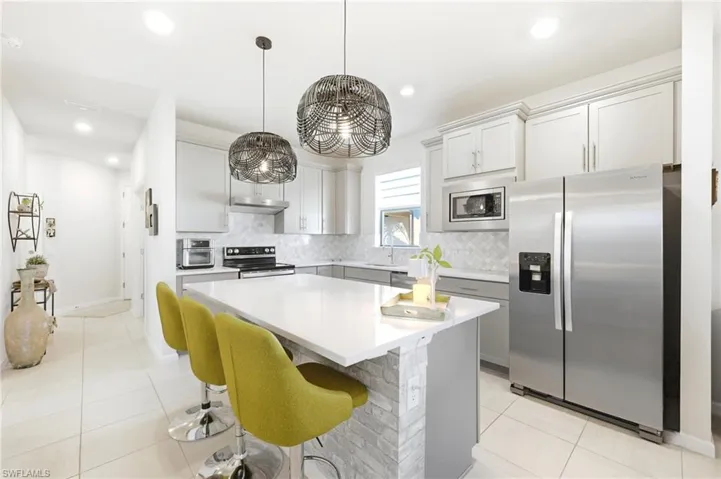 Modern kitchen featuring a central island with white countertop, pendant lighting, stainless steel appliances, light gray cabinetry, and tile flooring