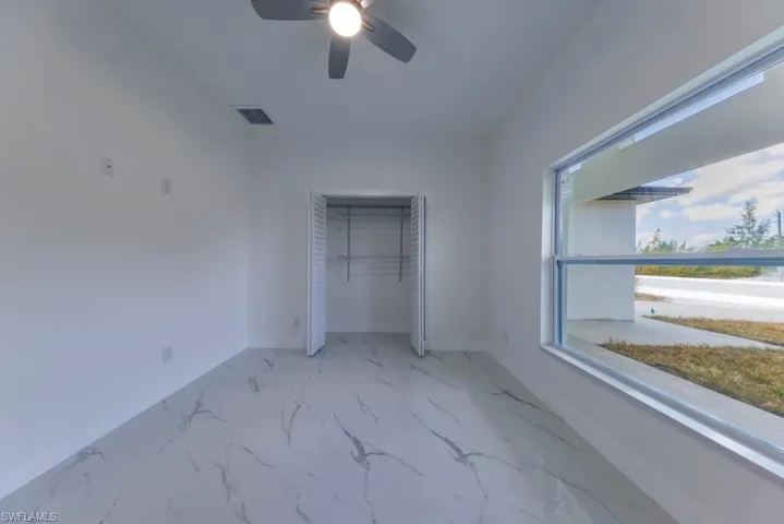 Unfurnished bedroom featuring a closet, light marble finish flooring, and ceiling fan