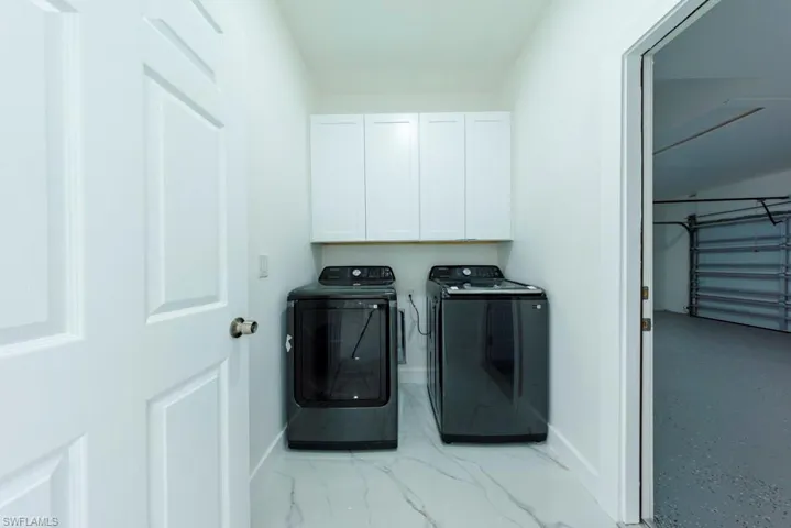 Laundry room featuring washer and dryer, cabinet space, and light marble finish flooring