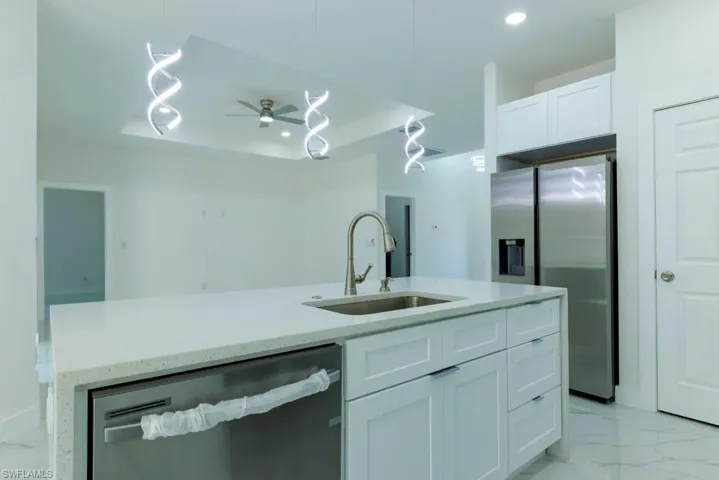 Kitchen featuring light marble finish floors, a raised ceiling, stainless steel appliances, light stone counters, and ceiling fan