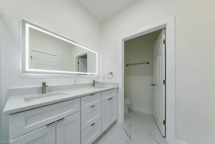 Full bath featuring double vanity and light marble finish floors