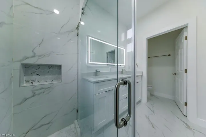 Bathroom featuring double vanity, light marble finish floors, and a marble finish shower
