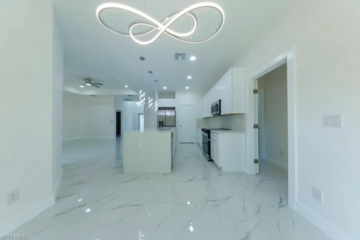 Kitchen featuring stainless steel appliances, an island with sink, open floor plan, white cabinets, and hanging lights