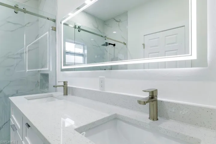 Full bathroom with double vanity and a marble finish shower