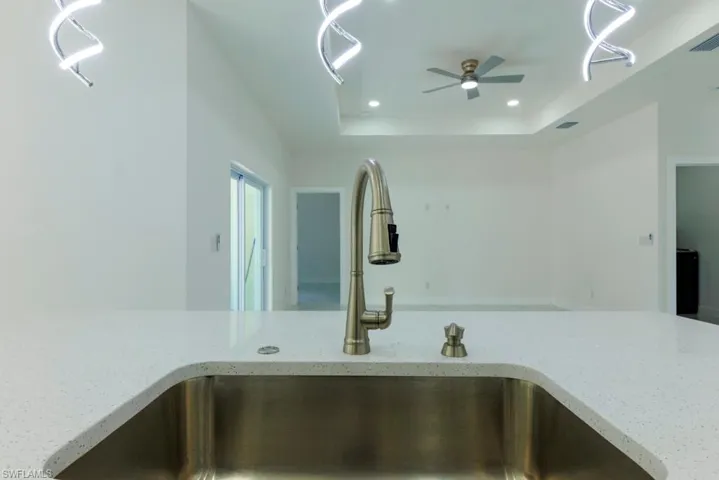 Kitchen view of light stone counters, ceiling fan, recessed lighting, and a tray ceiling