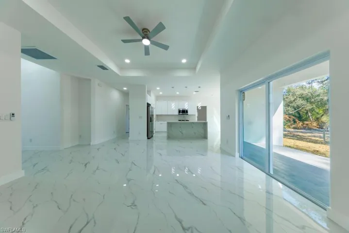 Unfurnished living room featuring a ceiling fan, a tray ceiling, recessed lighting, and light marble finish flooring