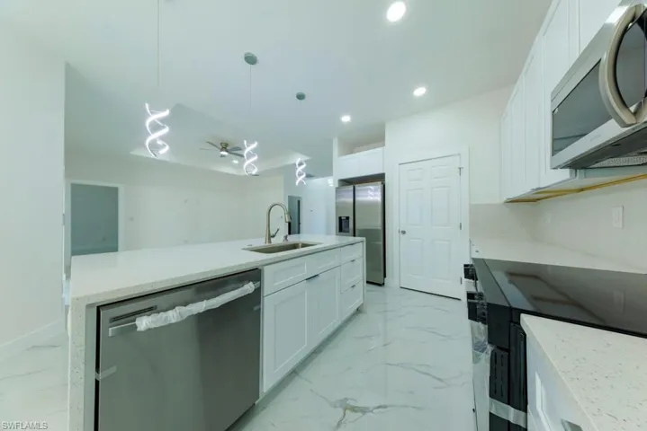 Kitchen with stainless steel appliances, light stone counters, hanging light fixtures, white cabinets, and light marble finish flooring