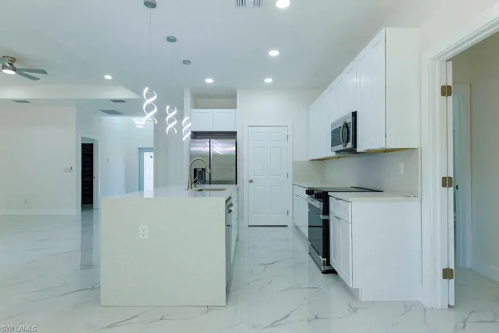 Kitchen with stainless steel appliances, decorative light fixtures, white cabinetry, light stone countertops, and a ceiling fan