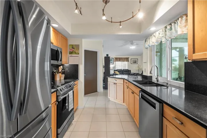 Kitchen featuring stainless steel appliances, sink, track lighting, ceiling fan, and a raised ceiling