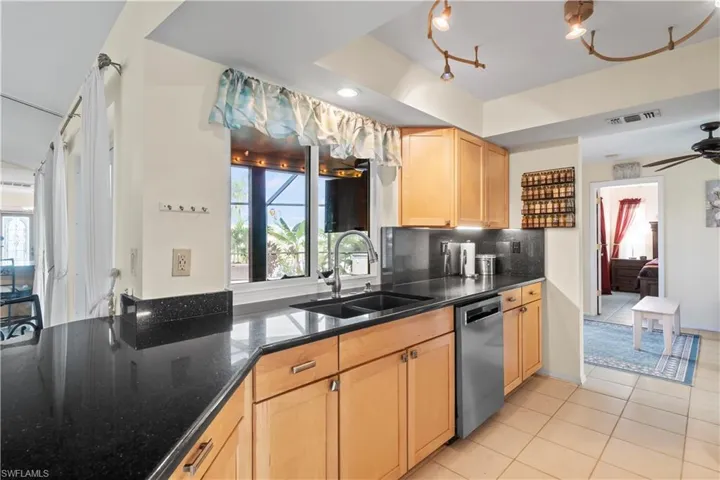 Kitchen with stainless steel dishwasher, backsplash, sink, ceiling fan, and light tile floors