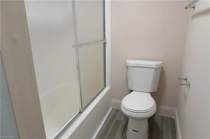 Bathroom with bath / shower combo with glass door, toilet, and wood-type flooring