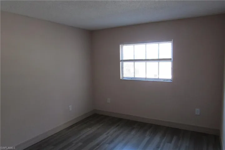 Empty room with dark hardwood / wood-style floors and a textured ceiling
