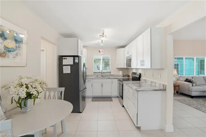 Kitchen featuring stainless steel appliances, white cabinets, light stone countertops, light tile patterned floors, and open floor plan - Virtually Edited Image