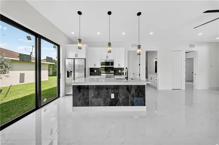 Kitchen with white cabinets, appliances with stainless steel finishes, backsplash, a large island, and light marble finish floors