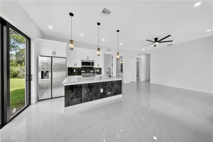 Kitchen with appliances with stainless steel finishes, decorative light fixtures, white cabinets, an island with sink, and backsplash