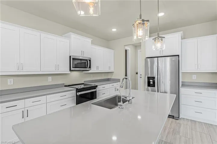 Kitchen with appliances with stainless steel finishes, white cabinets, decorative light fixtures, a kitchen island with sink, and recessed lighting