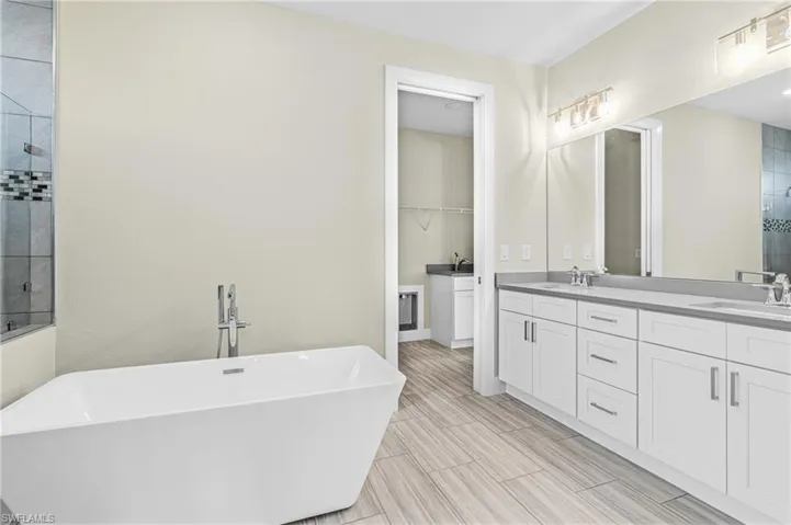 Full bath featuring a tile shower, a freestanding bath, double vanity, and a spacious closet