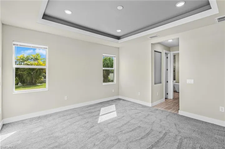Spare room with a tray ceiling, light carpet, and recessed lighting
