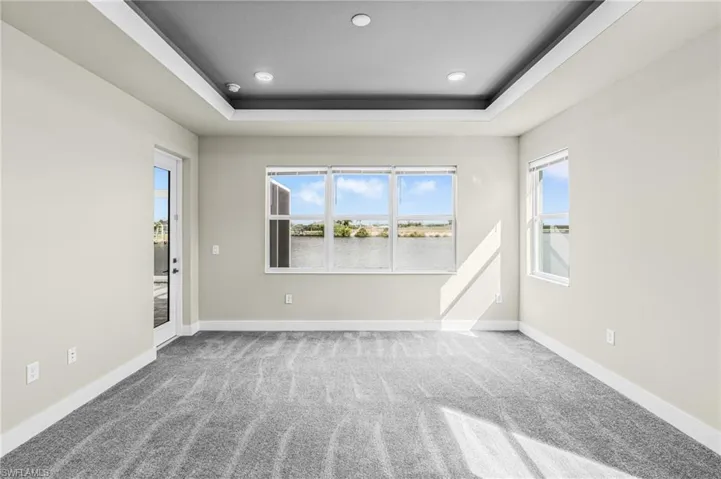 Carpeted spare room featuring a raised ceiling, healthy amount of natural light, a water view, and recessed lighting