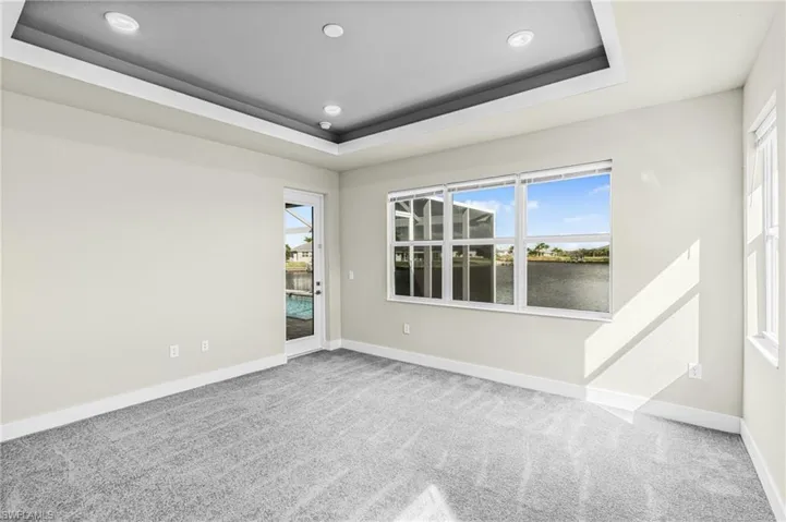 Carpeted empty room featuring a raised ceiling, a water view, healthy amount of natural light, and recessed lighting