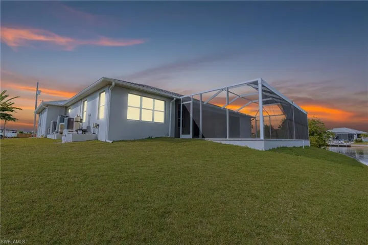Back of house with a sunroom, a lanai, a yard, and stucco siding