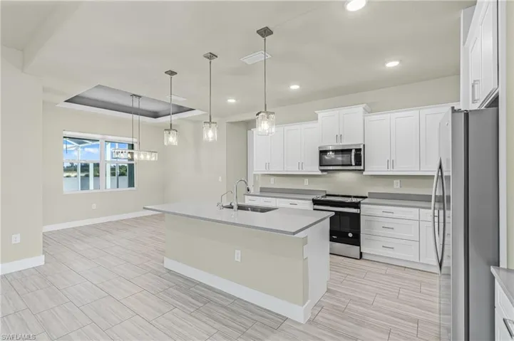 Kitchen with appliances with stainless steel finishes, an island with sink, white cabinets, decorative light fixtures, and recessed lighting
