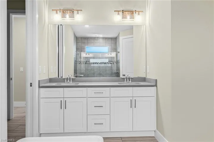 Bathroom featuring a shower stall, double vanity, and wood tiled floors