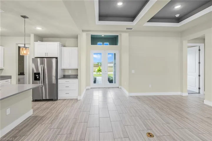 Kitchen featuring white cabinetry, stainless steel refrigerator with ice dispenser, french doors, a raised ceiling, and pendant lighting