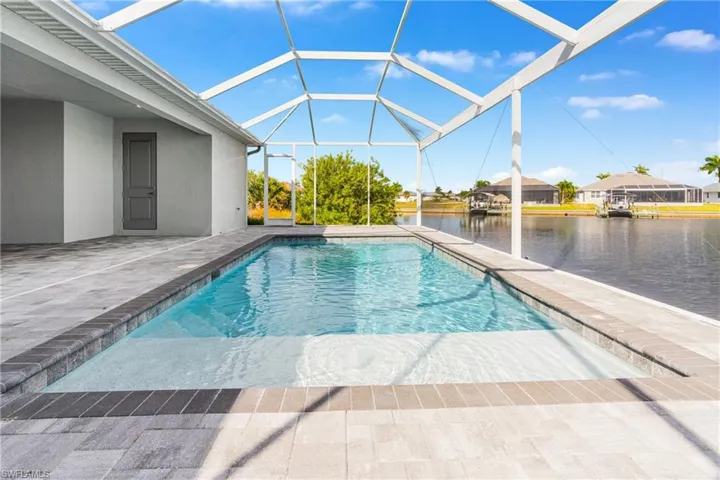 Outdoor pool with a sunroom, a patio area, a water view, and glass enclosure