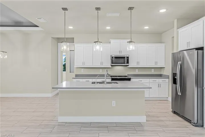 Kitchen featuring appliances with stainless steel finishes, recessed lighting, decorative light fixtures, white cabinets, and a kitchen island with sink
