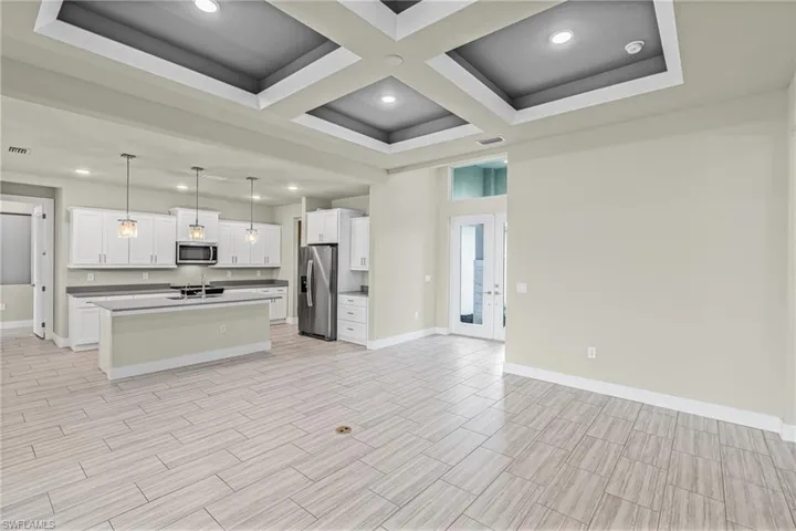 Kitchen featuring coffered ceiling, hanging light fixtures, open floor plan, appliances with stainless steel finishes, and white cabinetry