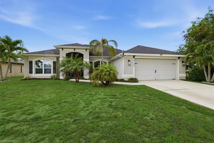 Stucco exterior architecture featuring a double garage, arched entry, and dark shingle roof