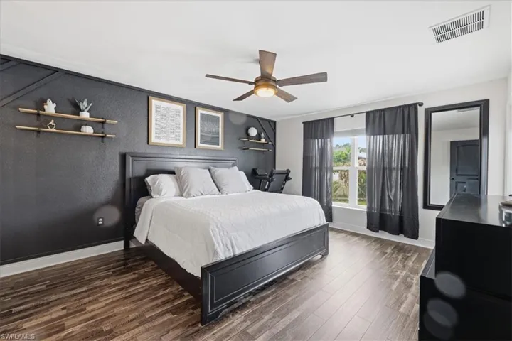 Spacious bedroom featuring wood-finish flooring, a contemporary ceiling fan, and a large window providing ample natural light