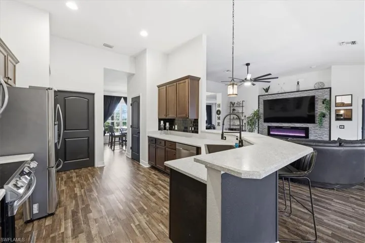 Modern kitchen featuring wood-finish flooring, stainless steel appliances, a light-colored countertop with an undermount sink, and a breakfast bar